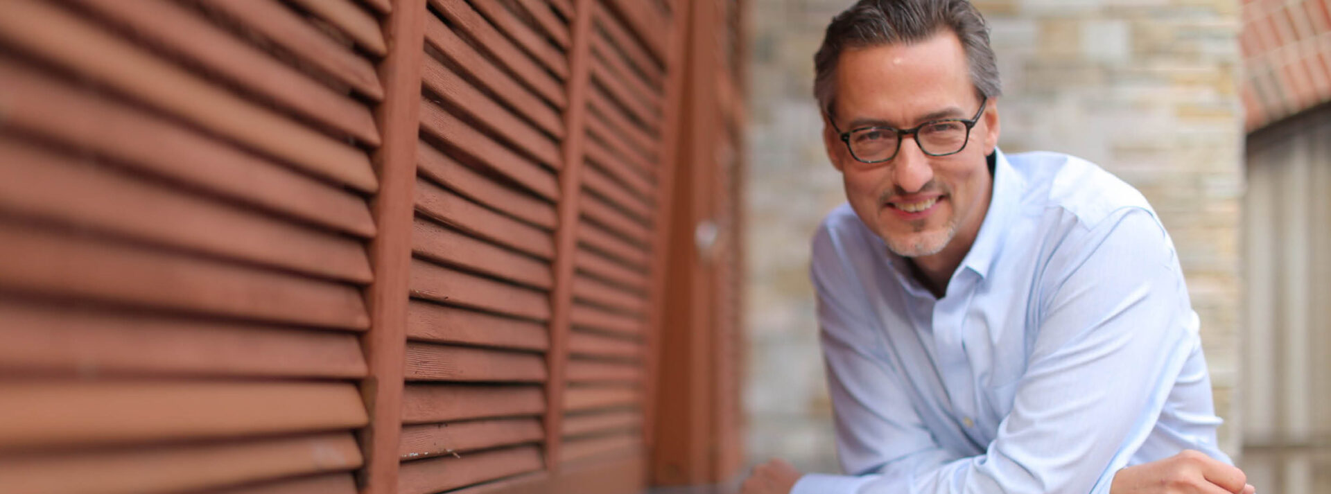 A man leaning against a wall with glasses on.